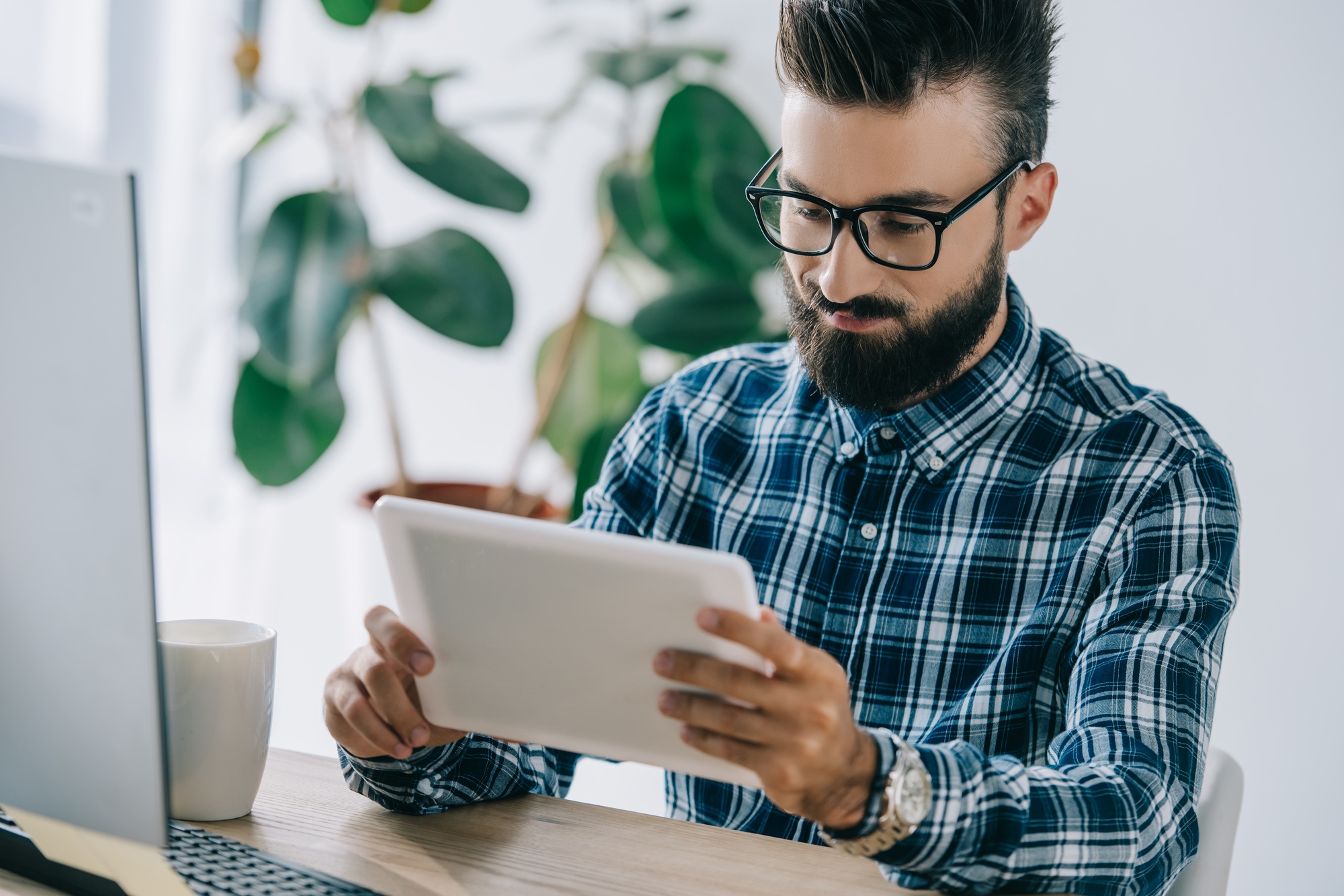 bearded young seo using tablet at workplace