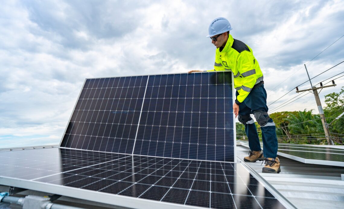 technician adjusts a solar panel on rooftop, emphasizing the transition to sustainable energy.